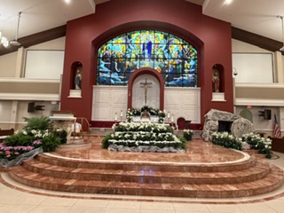The sanctuary of Our Lady Queen of Apostles with the altar, crucifix and stained-glass window decorated with white flowers